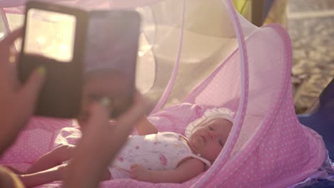 Mom-with-mobile-taking-picture-of-baby-in-bassinet-outdoor