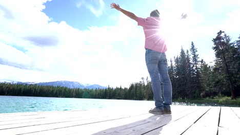 Young-man-arms-outstretched-on-lake-pier,-Canada