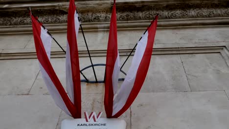 tracking-shot-from-Austrian-flags-towards-carved-column-of-Karlsplatz-church,-Vienna-Austria