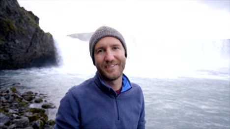 Portrait-of-young-man-tourist-traveling-with-magnificent-waterfall-in-Iceland