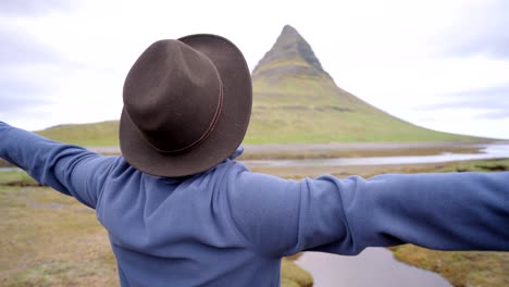 4K---Young-man-in-Iceland-arms-outstretched-for-freedom-Springtime-overcast-sky-at-famous-Kirkjufell-mountain