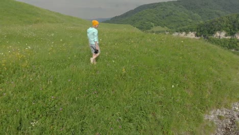 The-girl-photographer-in-glasses-and-a-hat-walks-with-her-dslr-camera-on-the-edge-of-the-plateau-near-the-precipice.-Aerial-view