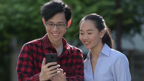 Young-Asian-couple-using-phone-together-outdoors