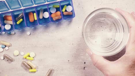 Tablets-in-the-organizer-and-on-the-table-and-a-glass-of-water-in-your-hand-top-view