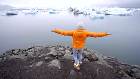 Young-woman-arms-outstretched-at-glacier-lagoon-in-Iceland-enjoying-freedom-in-nature