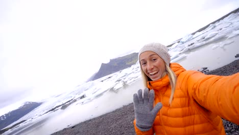 Slow-motion-Young-woman-taking-selfie-with-glacier-lake,-icebergs-floating-on-water