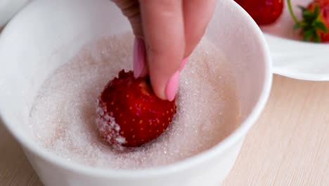 Woman-dips-the-strawberries-in-the-sugar.-Close---up-woman's-hand-next-to-a-plate-of-strawberries.