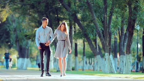 Young-couple-walking-along-the-city-park-together,-go-to-the-camera