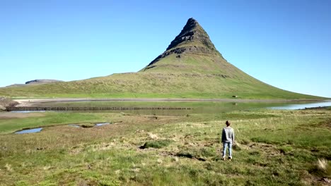 Vista-aérea-de-Drone-de-brazos-mujer-caucásica-levantados-para-las-emociones-positivas,-montaña-de-Kirkjufell-sobre-fondo.-Rodada-en-Islandia-occidental,-primavera.-La-gente-viaja-despreocupado-estilo-de-vida-concepto---4K