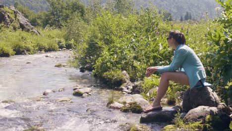 Traveling-woman-sitting-on-river-shore-and-enjoying-beautiful-landscape