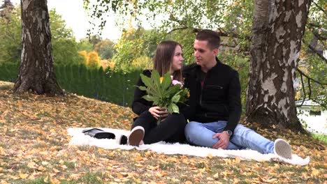 A-young-couple-sits-on-a-white-bedspread-in-autumn-park