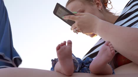 Mamá-con-bebé-durmiendo-en-la-playa.-Mujer-con-teléfono-móvil