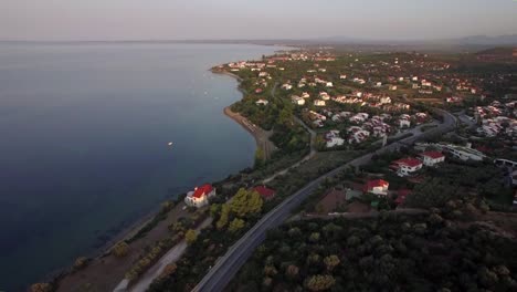 Volando-sobre-Costa-de-Trikorfo-Beach-con-casas-y-tierras-verdes,-Grecia