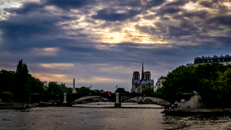 Timelapse-de-barcos-iluminados-en-París-por-la-noche,-con-la-Catedral-de-Notre-Dame-De-París-en-el-fondo,-vista-desde-el-puente-de-Henri-II