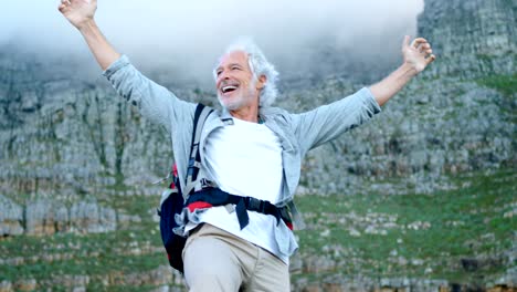 Senior-man-standing-with-arms-up-on-a-rock-at-countryside-4k