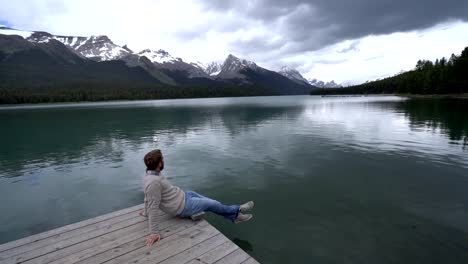 Hombre-joven-en-el-muelle-del-lago-mirando-el-paisaje-de-montaña-en-Canadá