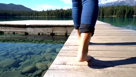 Closed-up-on-woman's-feet-walking-on-wooden-pier-above-stunning-mountain-lake-scenery