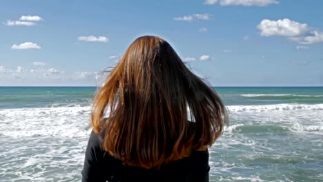 Chica-con-pelo-largo-rojo-en-la-playa,-brisa-juega-con-el-pelo,-tiro-durante-el-día.