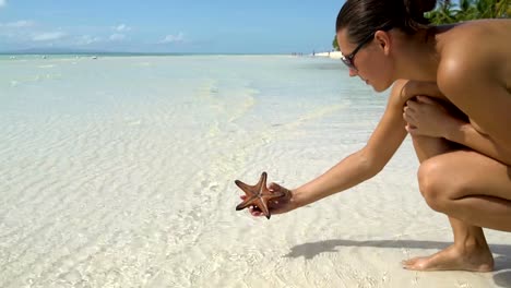 A-woman-in-a-bathing-suit-takes-a-starfish-and-puts-it-back