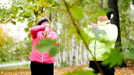 Mature-woman-in-colourful-jackets-doing-gymnastics-in-an-autumn-park-after-a-scandinavian-walk