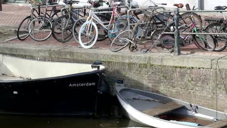 zahlreiche-Fahrräder-und-der-Bug-eines-Bootes-an-einem-Kanal-in-amsterdam