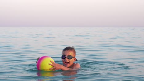 Glückliches-Kind-Baden-im-Meer-mit-ball