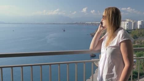 Frau-mit-Telefon-reden-und-genießen-Sie-Meerblick-vom-Balkon