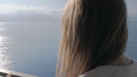 Eine-Frau-auf-einem-Balkon,-Telefon-und-Blick-aufs-Meer-hinter-ihr-im-Gespräch