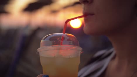 Frau,-die-Eistee-trinken-am-Strand-bei-Sonnenuntergang