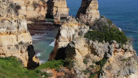 Ponta-da-Piedade,-lugar-famoso-en-el-sur-de-Portugal,-la-ciudad-de-lagos,-la-costa-rocosa,-olas-de-océano-Atlántico,-rocas-afiladas,-agua-azul,-flores-amarillas,-arco,-nadie,-playa-salvaje