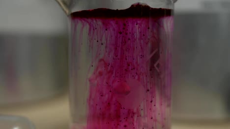 Cerrar-vista-de-vaso-de-precipitados-de-laboratorio-con-disolución-de-colorante-rojo.-Líquido-de-color-rosado-o-rojo-se-disuelve-en-el-matraz