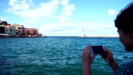 Young-woman-takes-the-photo-a-lighthouse-in-a-European-city-uses-smartphone