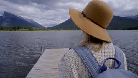 Young-woman-walking-on-wooden-pier-on-a-stunning-lake,-woman-contemplating-nature.-Stunning-mountain-lake-scenery