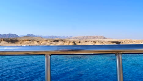 summer,-sea,-through-a-metal-fence-on-the-deck-you-can-see-a-beautiful-seascape.-deserted-shore,-tents-and-machines-of-Bedouins