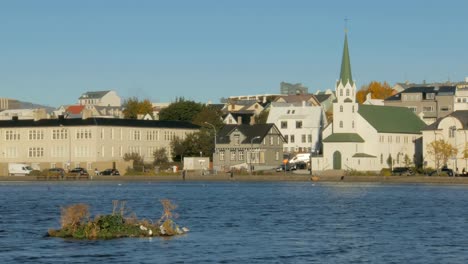 Blick-auf-alte-traditionelle-Gebäude-in-der-Nähe-von-Lake-Tjörnin-in-Reykjavik-im-sonnigen-Herbsttag