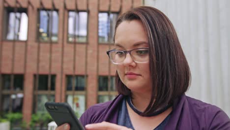 Señora-joven-llevando-gafas-usar-teléfono-en-la-ciudad