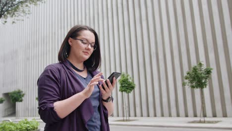 Señora-joven-llevando-gafas-usar-teléfono-en-la-ciudad