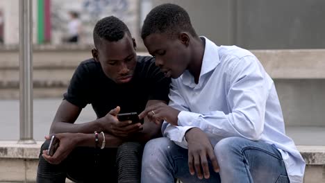 Two-young-african-black-men-focused-on-smartphone-in-the-street