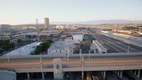 Toma-aérea-del-río,-carretera-y-edificios-en-el-centro-de-Los-Ángeles-durante-la-puesta-de-sol