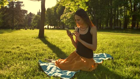 Junge-Dame,-die-Natur-und-den-Sonnenuntergang-zu-genießen.-Sitzen-auf-grüne-Sommerpark-mit-mobilen