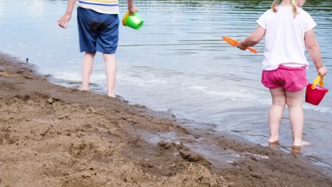 Kleine-Mädchen-und-jungen-ziehen-Wasser-aus-dem-Fluss-mit-einem-Eimer,-langsamen-Satz.-Kinder-spielen-in-der-Natur-in-den-Sand-am-Strand