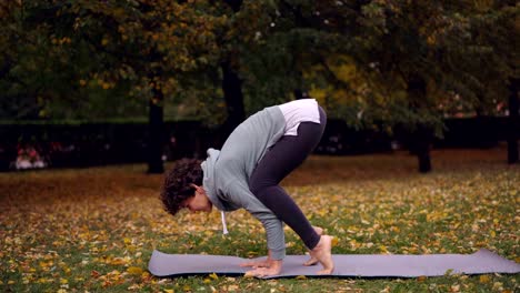 Beautiful-brunette-is-practising-Bakasana-balancing-on-hands-on-yoga-mat-exercising-alone-in-park.-Modern-youth,-recreational-activity-and-leisure-concept.