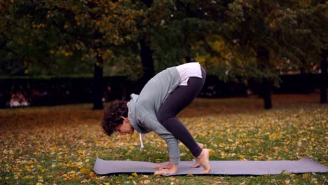 Preciosa-morena-practica-Bakasana-equilibrio-sobre-las-manos-en-la-colchoneta-de-yoga-ejercicio-solo-en-el-parque.-Juventud-moderna,-concepto-de-ocio-y-actividad-recreativa.