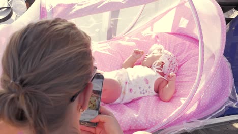 Babymädchen-in-rosa-Stubenwagen-und-Mutter-Surfen-auf-Zelle-im-freien