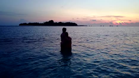 v04157-Aerial-flying-drone-view-of-Maldives-white-sandy-beach-2-people-young-couple-man-woman-romantic-love-sunset-sunrise-on-sunny-tropical-paradise-island-with-aqua-blue-sky-sea-water-ocean-4k