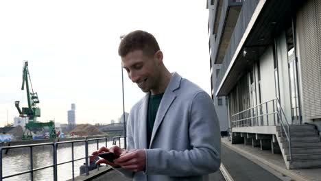 Glücklicher-Mann-mit-Handy-bei-einer-industriellen-Pier