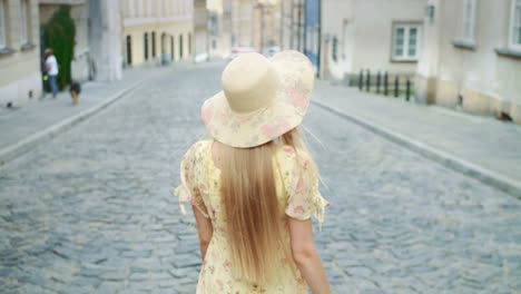 Smiling-woman-walking-on-street.-Cheerful-pretty-woman-in-white-hat-looking-back-at-camera-while-walking-in-town