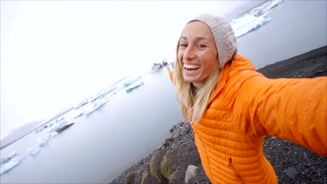 Retrato-de-selfie-de-vídeo-lenta-de-mujer-joven-de-pie-junto-a-la-laguna-glaciar-en-Islandia