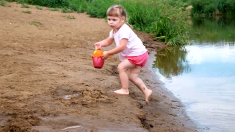 Kleine-Mädchen-holt-und-gießt-Wasser-aus-dem-Eimer-in-den-Sand.-Kinder-spielen-am-Strand