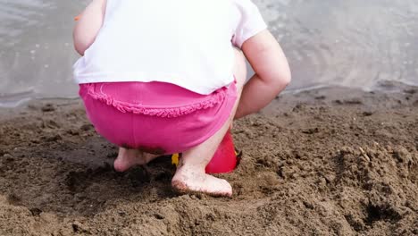 Niña-está-tocando-una-paleta-en-el-cubo,-cámara-lenta.-Niño-juega-en-la-naturaleza-en-la-arena-de-la-playa